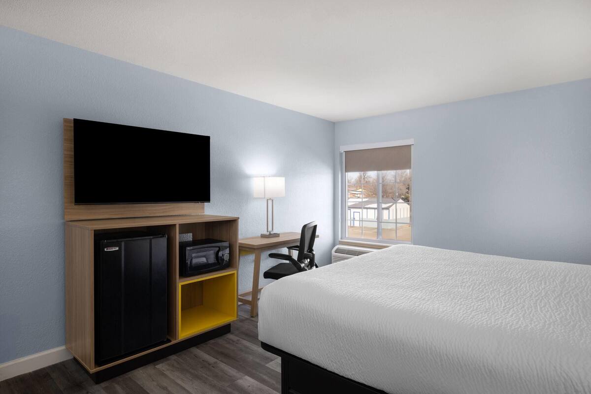 A hotel room with a bed, a TV, a desk with a chair, a lamp, and a window with a view.