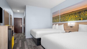 A hotel room with two beds, a TV, a wooden cabinet, and a wall art of sunflowers.