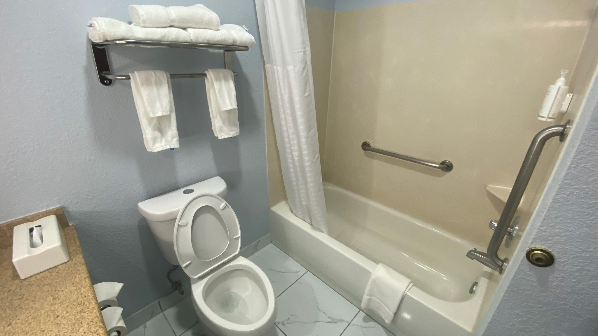 A bathroom with a toilet, a shower with a grab bar, and a towel rack.