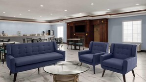 A spacious lounge area with a blue sofa set, a glass coffee table, and a dining area with chairs and a table.