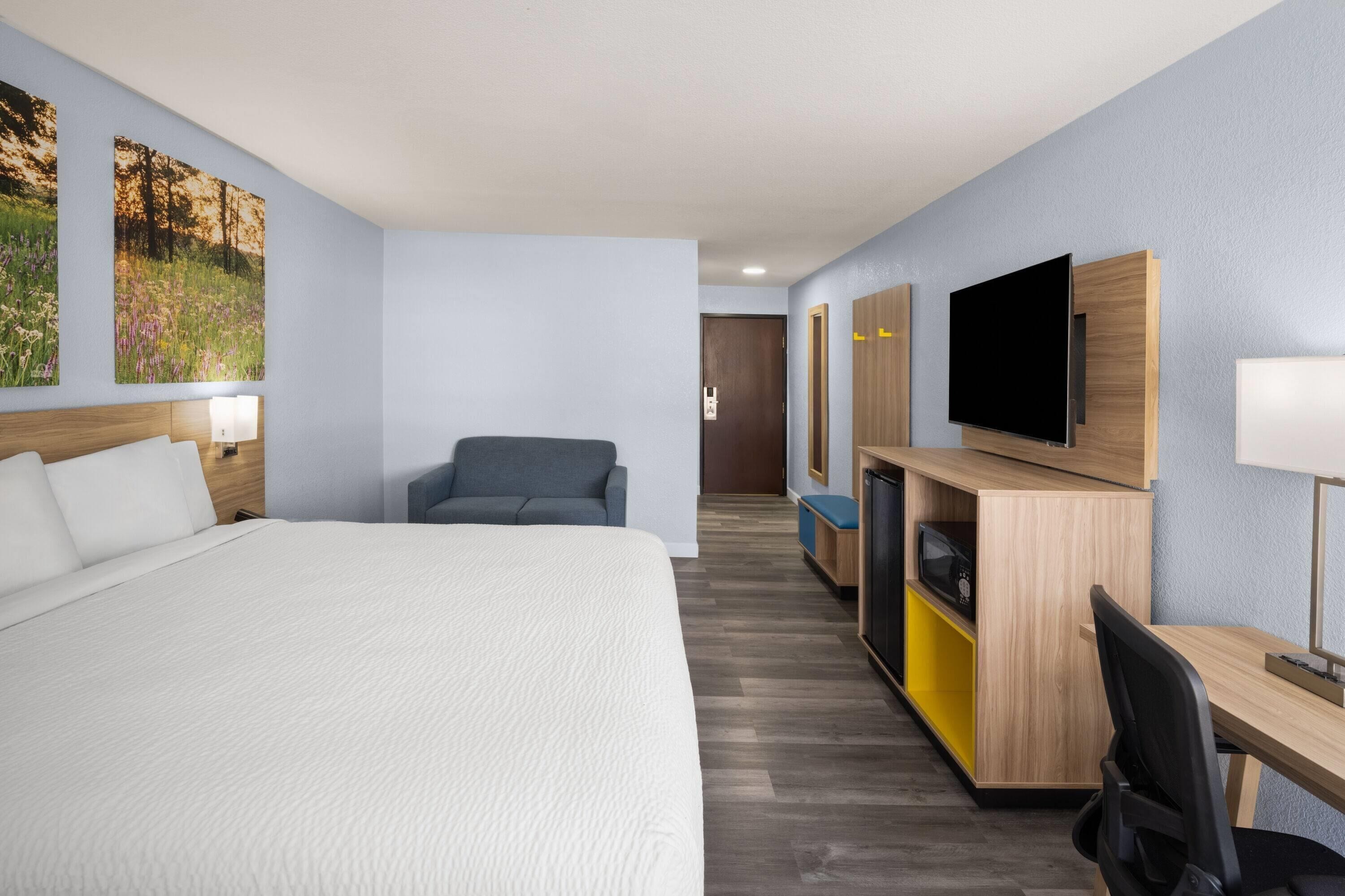 A hotel room with a large bed, a desk with a flat-screen TV, a gray sofa, and a wooden cabinet with a microwave.