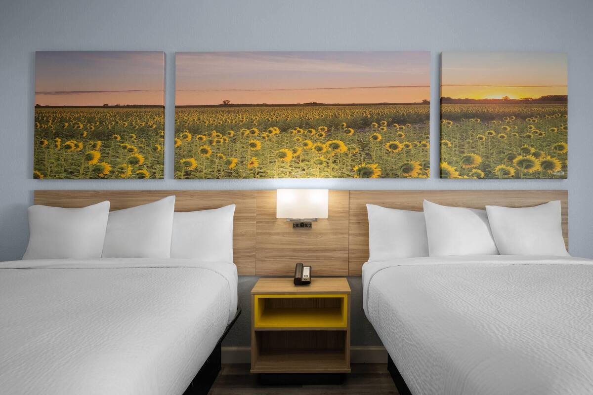A hotel room with two beds, a nightstand, and a wall-mounted light.