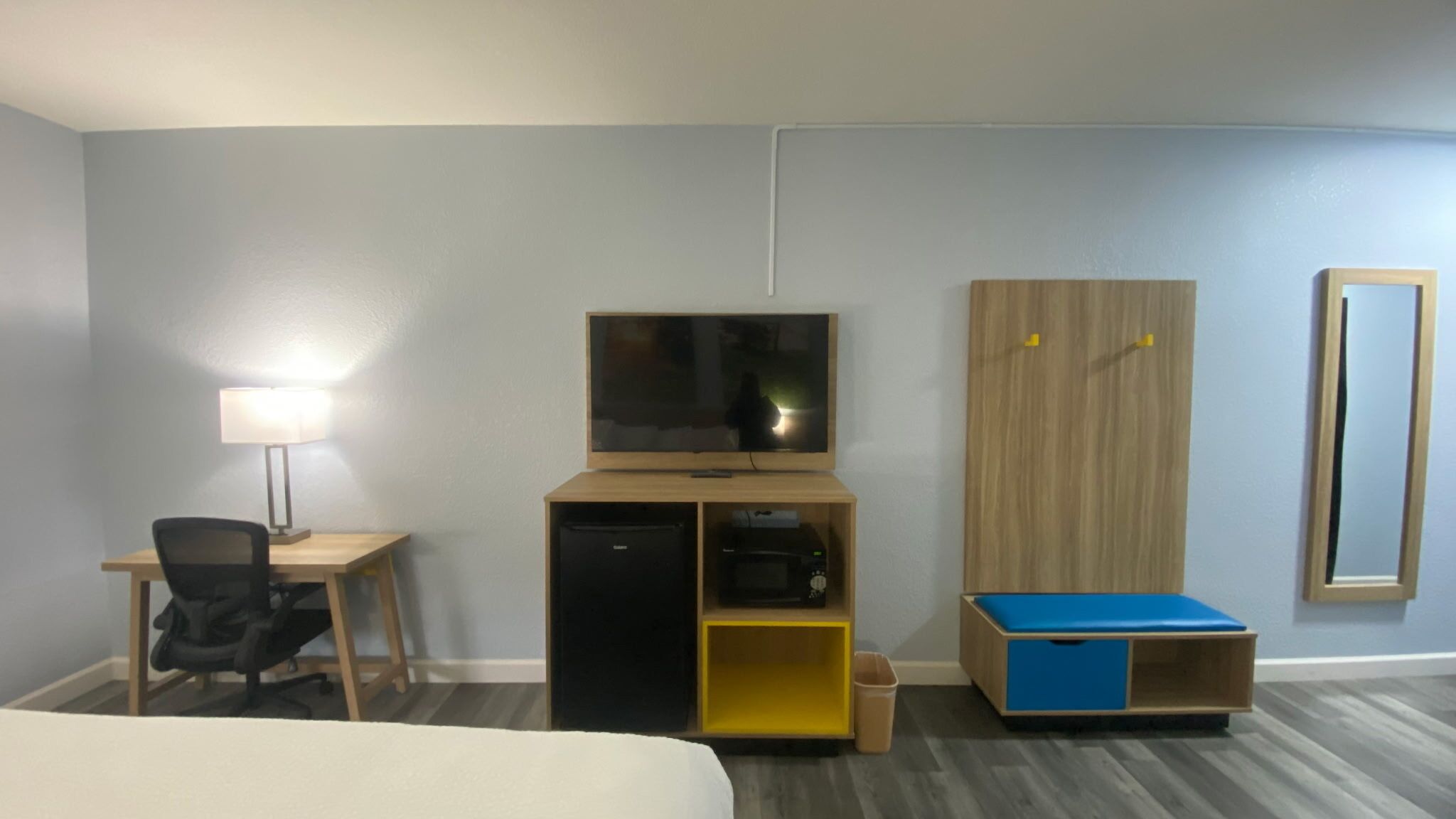 Habitación de hotel con cama, escritorio con lámpara, televisor, armario y un pequeño mueble azul para guardar objetos.