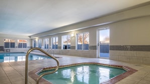 An indoor swimming pool with a tiled deck, a metal pool ladder, and a view of the outside through large windows.
