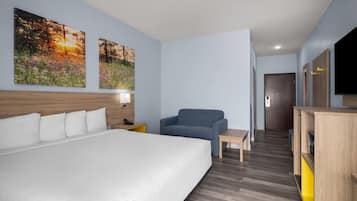 A hotel room with a large bed, a sofa, a small table, and a TV. There are two paintings on the wall and a wooden headboard.