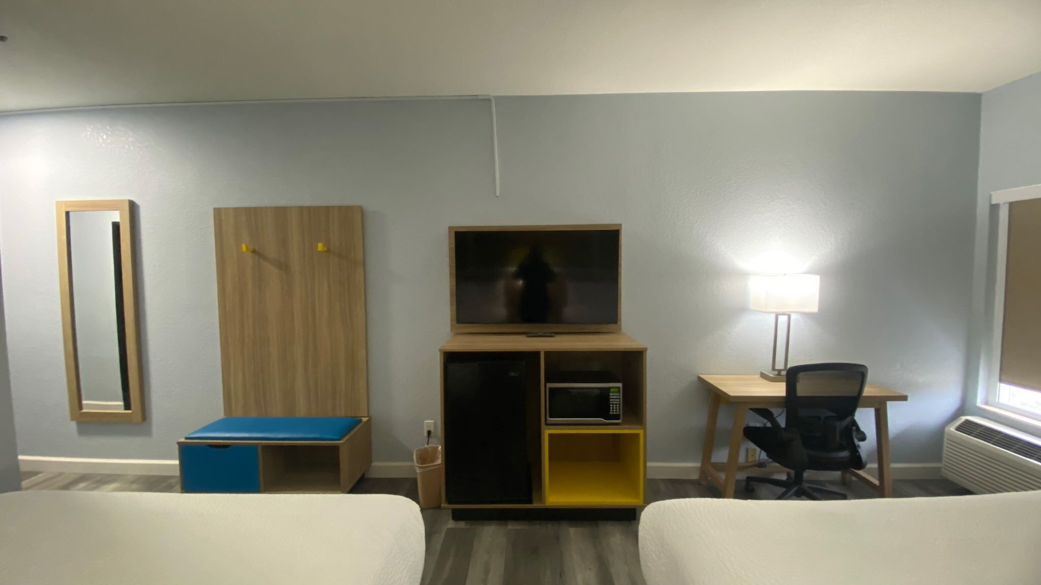 Quarto de hotel com duas camas, uma escrivaninha com cadeira, televisão, micro-ondas e um pequeno armário.