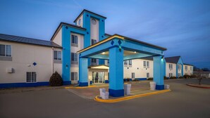 A hotel with a blue and white exterior, a covered entrance, and a parking lot.