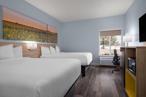 Una habitación de hotel con dos camas, un cuadro grande de girasoles, un televisor y un escritorio con una lámpara.