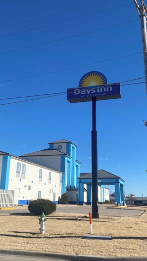 Letrero de Days Inn con un logo de sol, un edificio de fachada azul y blanca, y un hidrante en primer plano.