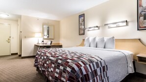 Een hotelkamer met een bed, een bureau, een stoel, een lamp, een spiegel en een schilderij aan de muur.
