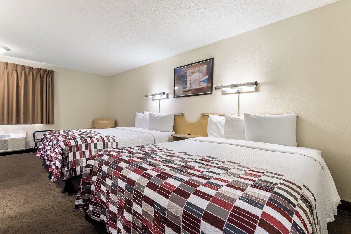 A hotel room with two beds, a desk, a chair, and a painting on the wall.