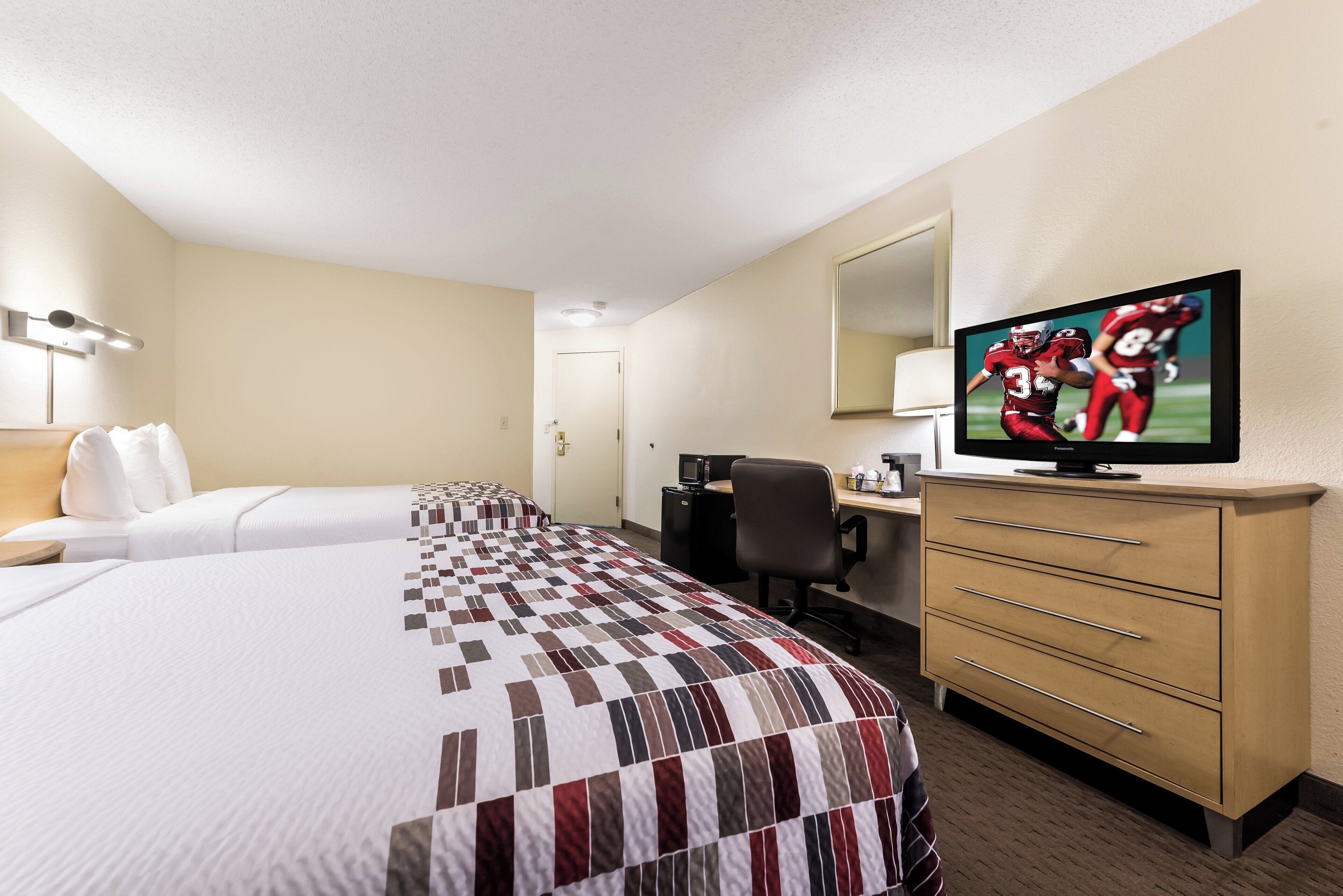 A hotel room with two beds, a desk, a chair, a television, and a minibar.
