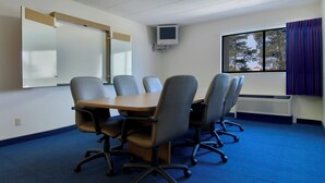 Een vergaderruimte met een tafel, stoelen, een whiteboard, een televisietoestel en een raam met gordijnen.