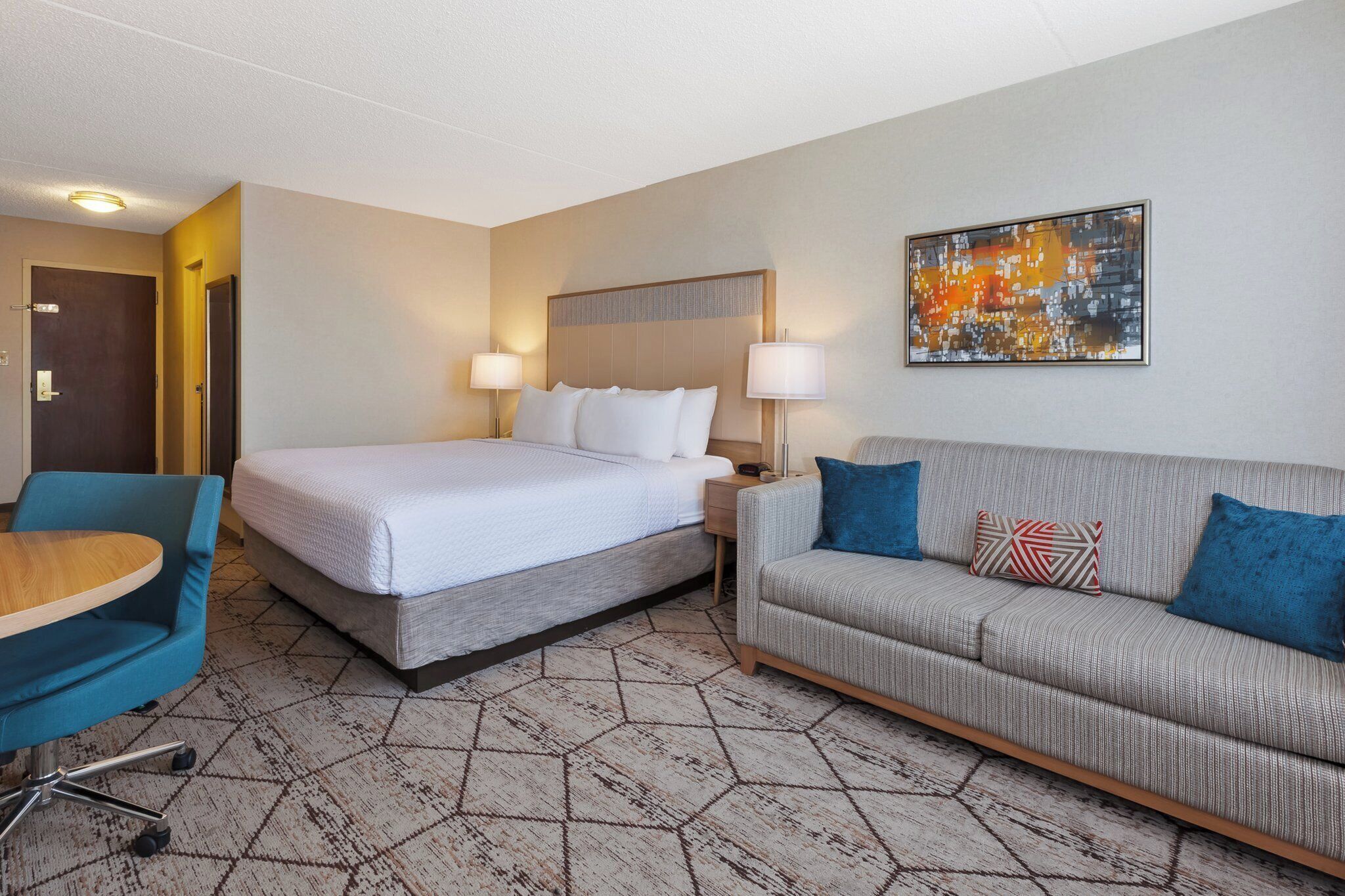 Une chambre d’hôtel avec un lit, un canapé, un bureau avec une chaise et un tableau au mur.