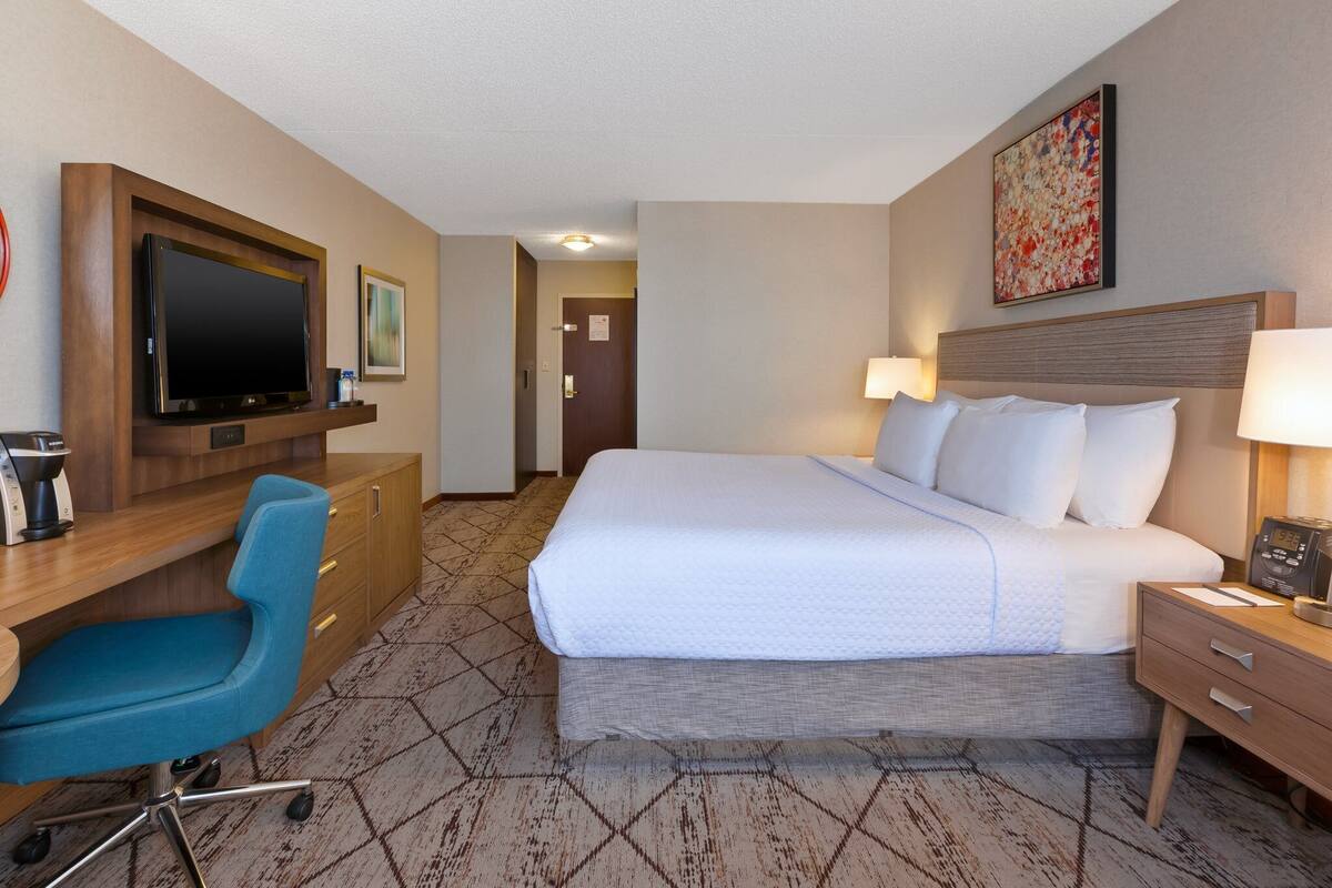 Una camera d'albergo con un letto, una scrivania, una sedia, una TV e opere d'arte alle pareti.