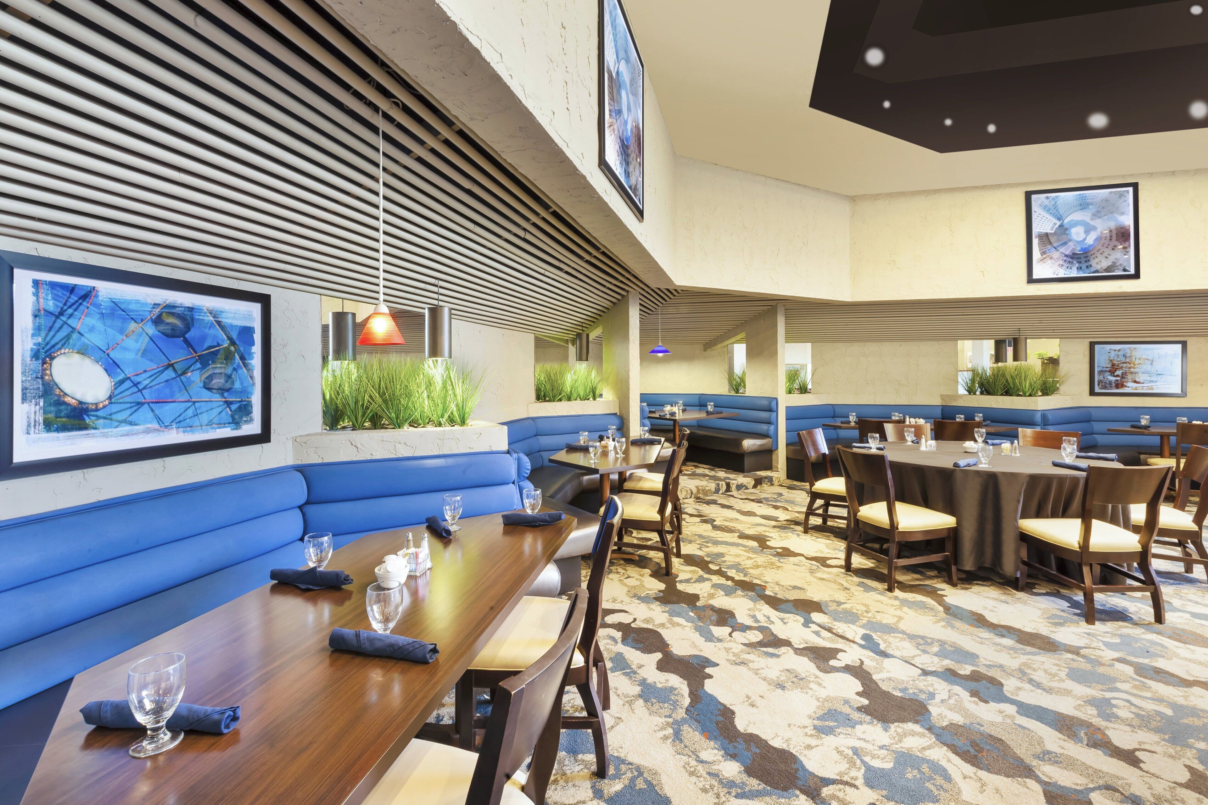 A restaurant with blue booths and tables, artwork on the walls, and a patterned carpet.