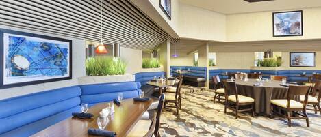 A restaurant with blue booths and tables, artwork on the walls, and a patterned carpet.