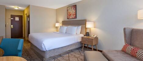 A hotel room with a bed, bedside lamps, a desk, a chair, and a sofa.