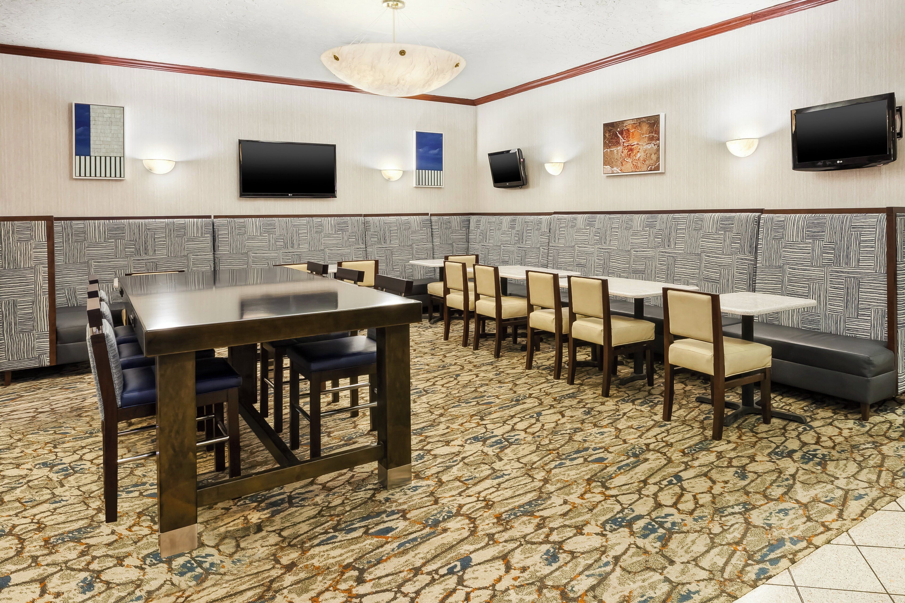 A conference room with a long table and multiple chairs, equipped with a flat-screen TV and wall-mounted speakers.