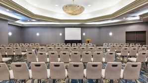 Een congreszaal met rijen stoelen, een projectiescherm en een tapijtvloer.
