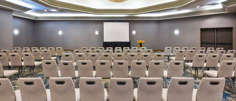 A conference room with rows of chairs, a projector screen, and a carpeted floor.