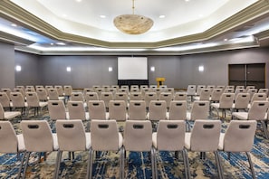 Une salle de conférence avec des rangées de chaises, un écran de projection et un sol recouvert de moquette.