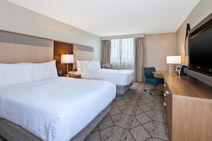 Quarto de hotel com duas camas, uma escrivaninha, televisão e uma cadeira.
