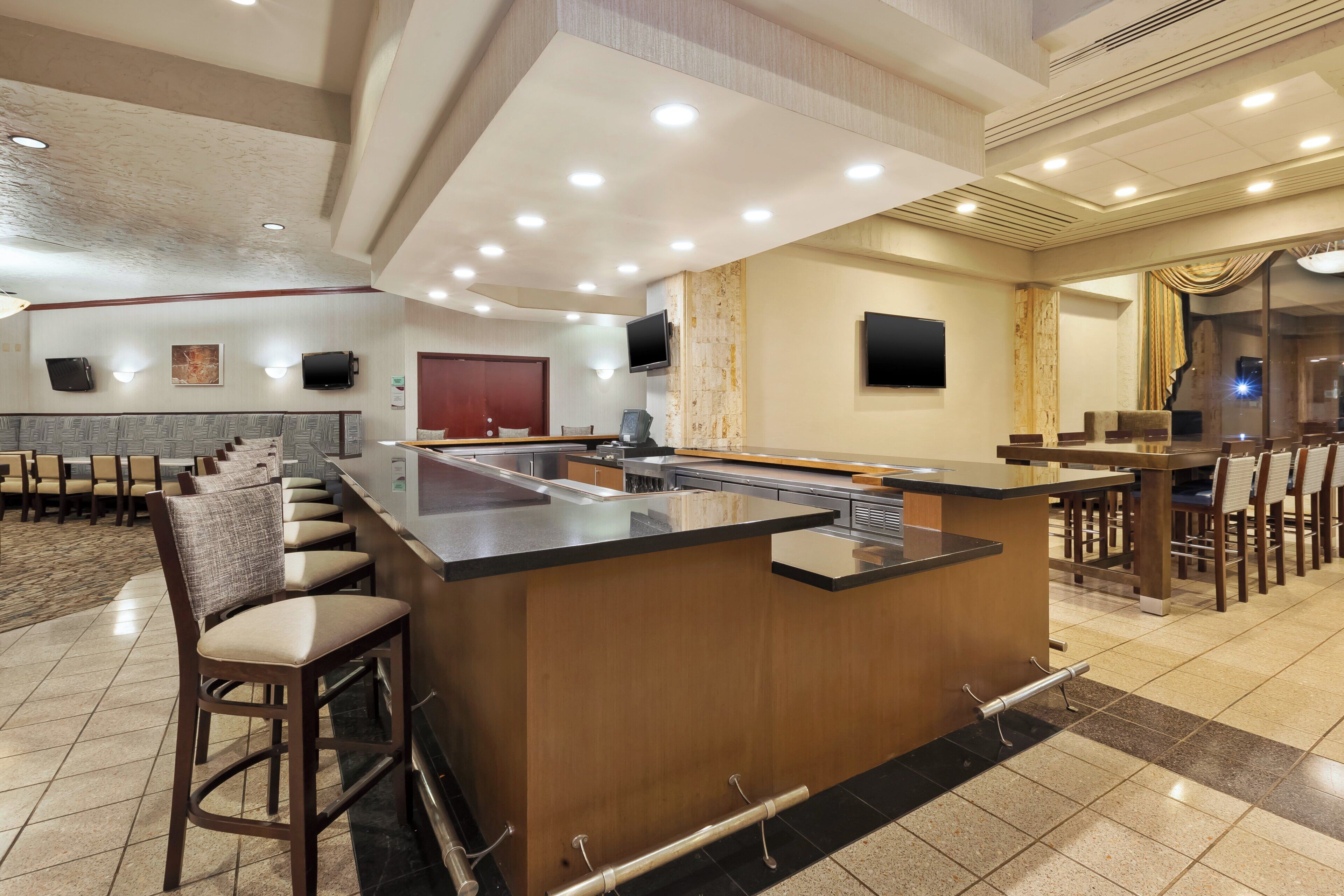 A hotel lobby with a bar area, seating arrangements, and a television screen.