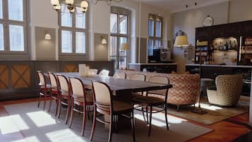 A dining area with a long table and chairs, a sofa, and a bar area with shelves of bottles and glasses.