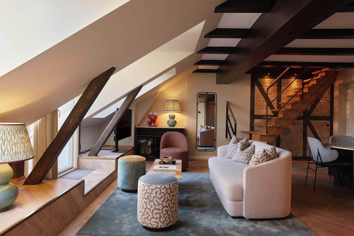 Un espacio habitable tipo loft con una escalera, un sofá, otomanas, una lámpara y una mesa de centro.