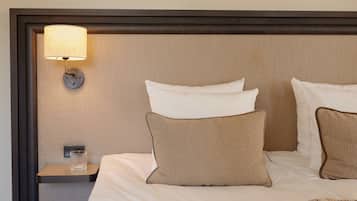 Una cama bien hecha con almohadas blancas y marrones, una mesita de noche con un vaso y una lámpara fijada a la pared.
