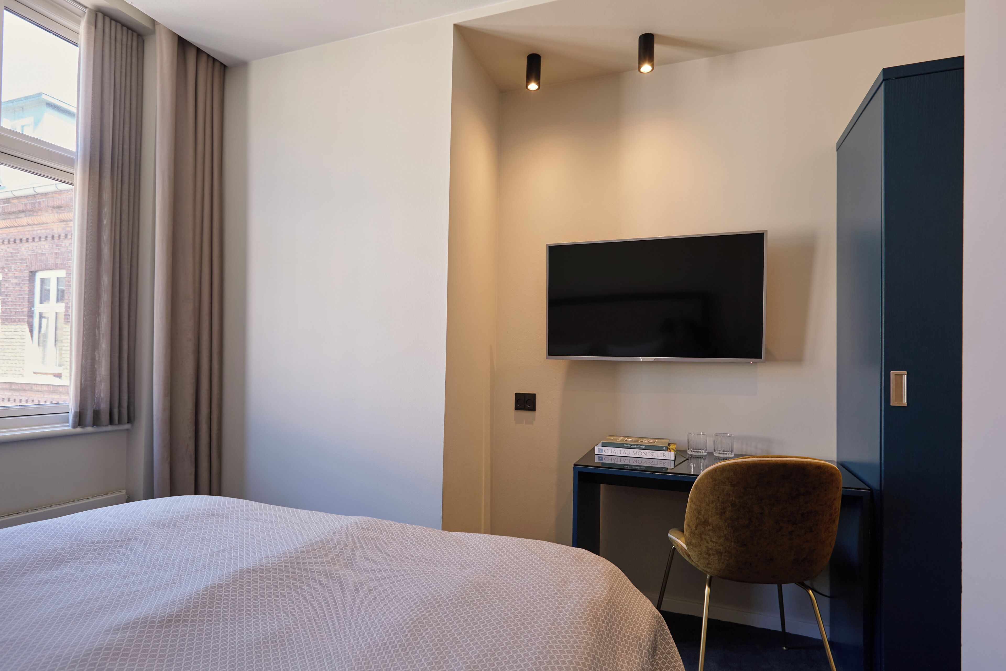 Habitación de hotel con cama, escritorio, silla, televisión de pantalla plana y armario.