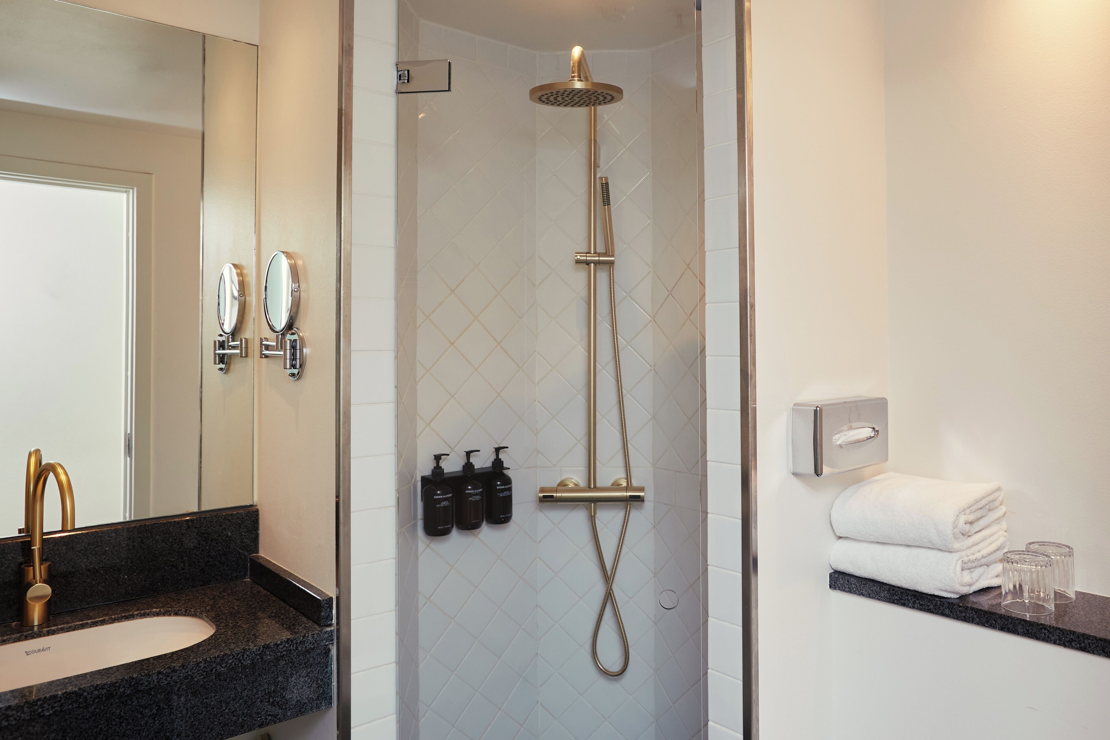 A bathroom with a sink, mirror, shower, and towel rack.