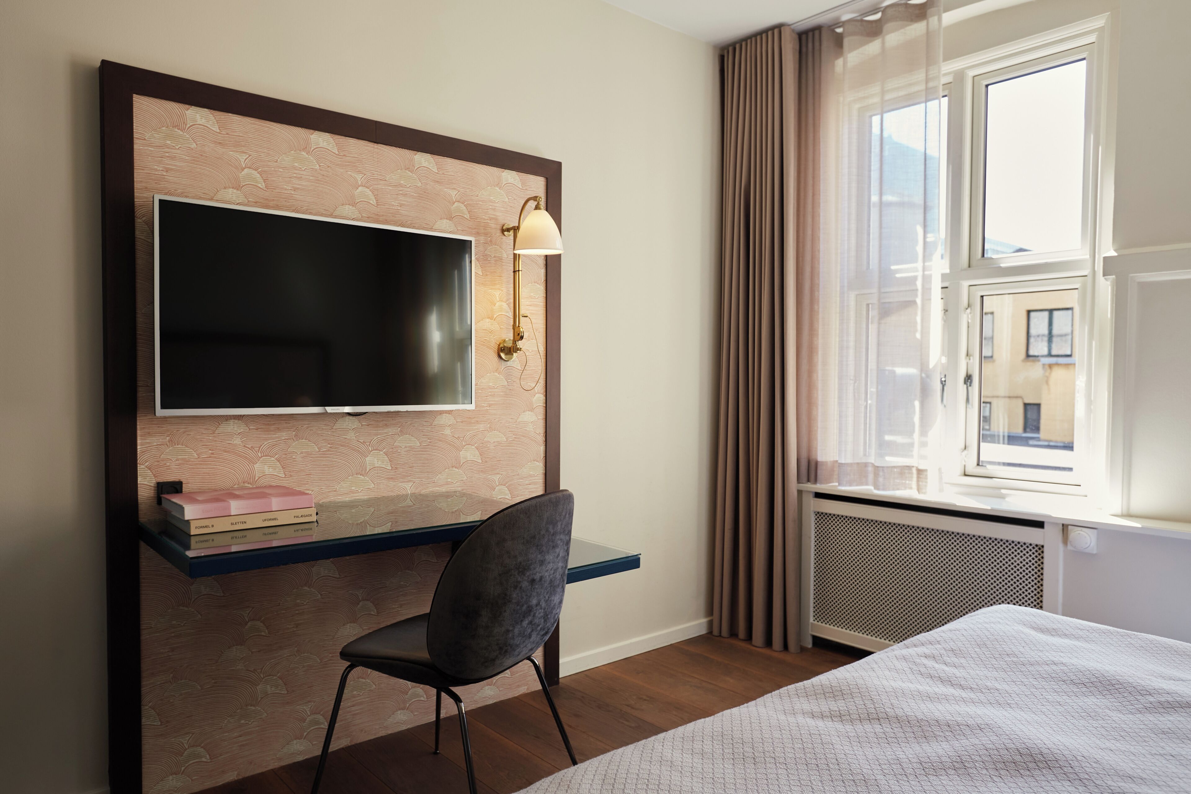 Une chambre d’hôtel comprenant un lit, un bureau avec une chaise, une télévision et une fenêtre avec des rideaux.
