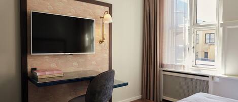 Una habitación de hotel con cama, escritorio con silla, televisión y ventana con cortinas.