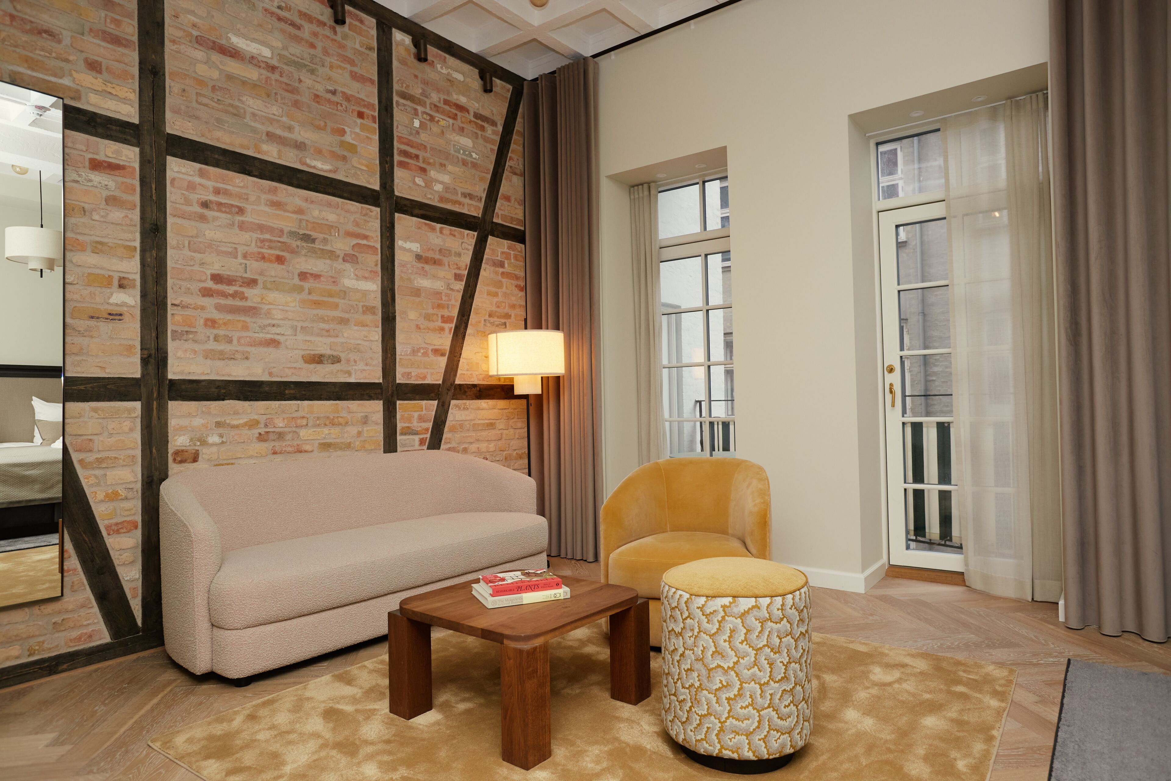 A living room with a brick wall, a sofa, a chair, a lamp, and a patterned ottoman.