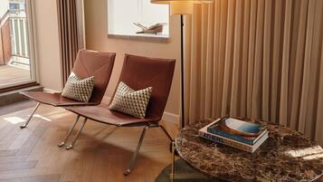Una habitación con dos sillones de cuero marrón con cojines estampados, una mesa redonda de mármol con un libro, una lámpara de pie y una ventana con persianas.