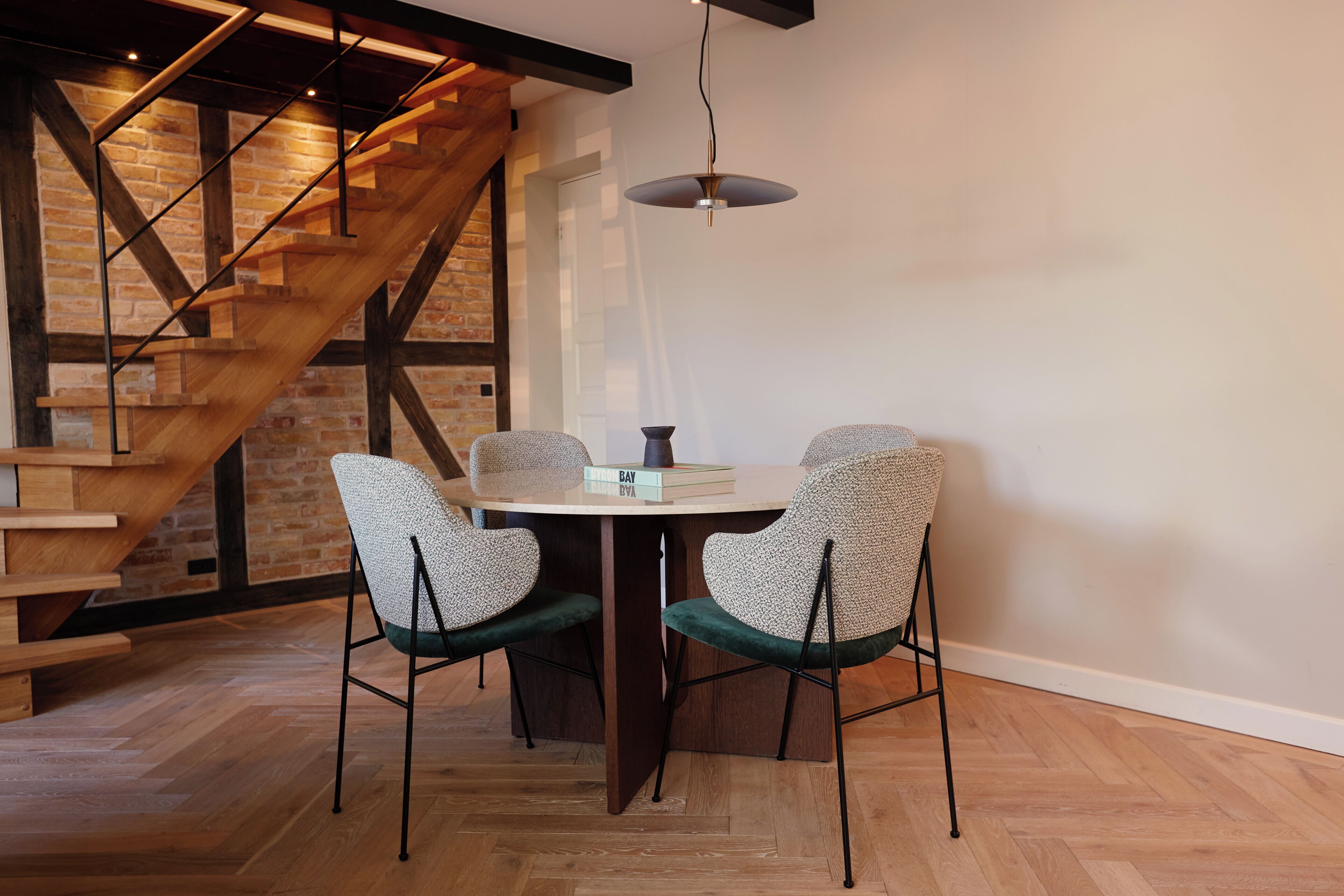 A dining area with a wooden table, two patterned chairs, a book, and a pendant light.