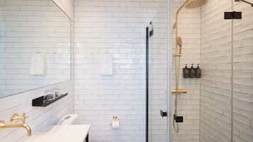 A modern bathroom with white tiled walls, a glass shower enclosure, a white sink, and gold fixtures.