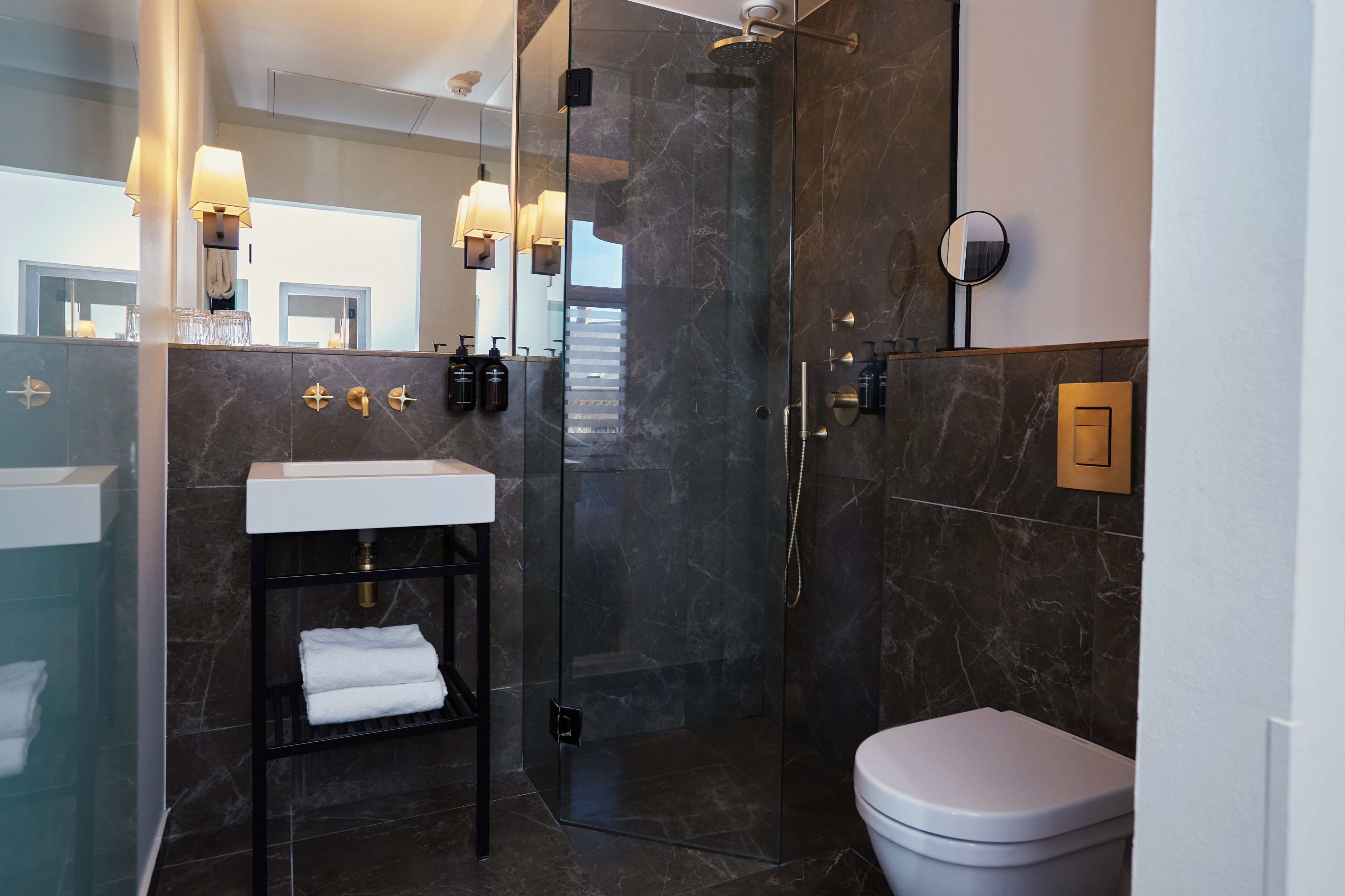 Een moderne badkamer met een glazen douchecabine, een witte wastafel en een toilet.
