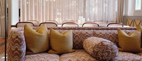 A patterned sofa with cushions, a lamp, and a window with curtains.