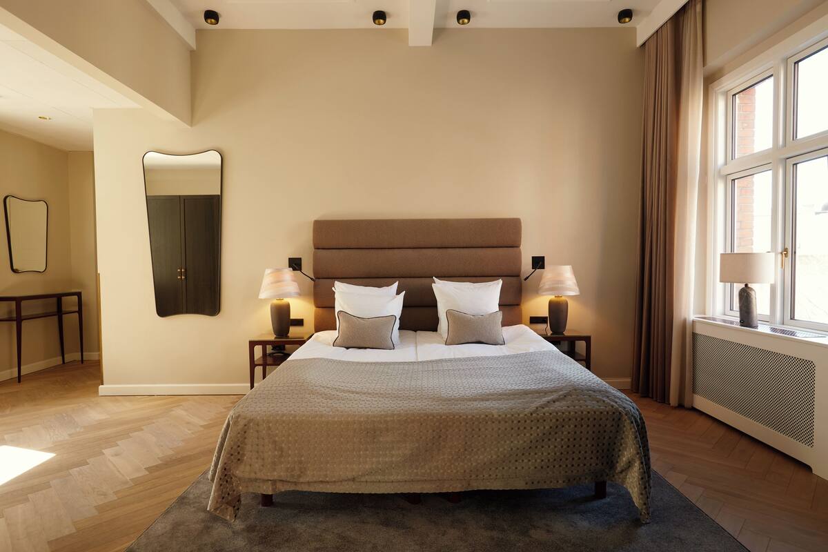 Un dormitorio con una cama grande, lámparas de noche, un espejo y una ventana con cortinas.