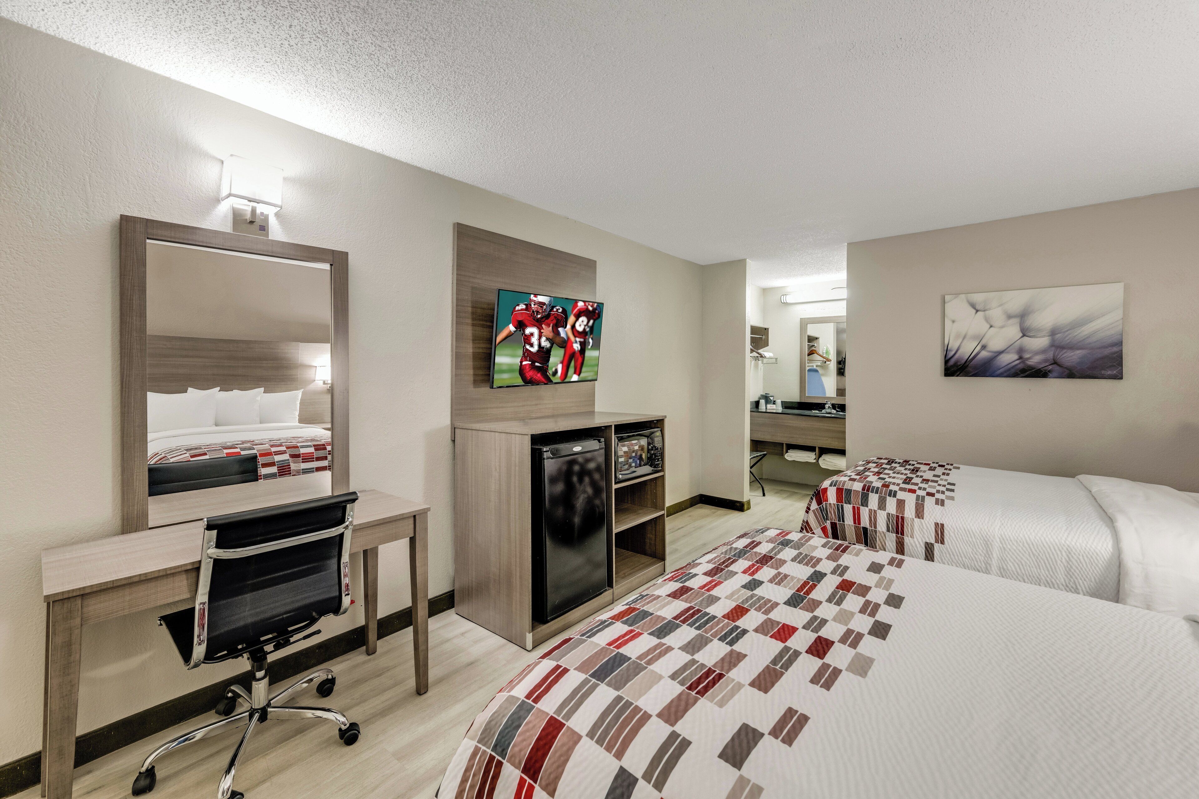 A hotel room with two beds, a desk, a chair, a television, and a refrigerator.