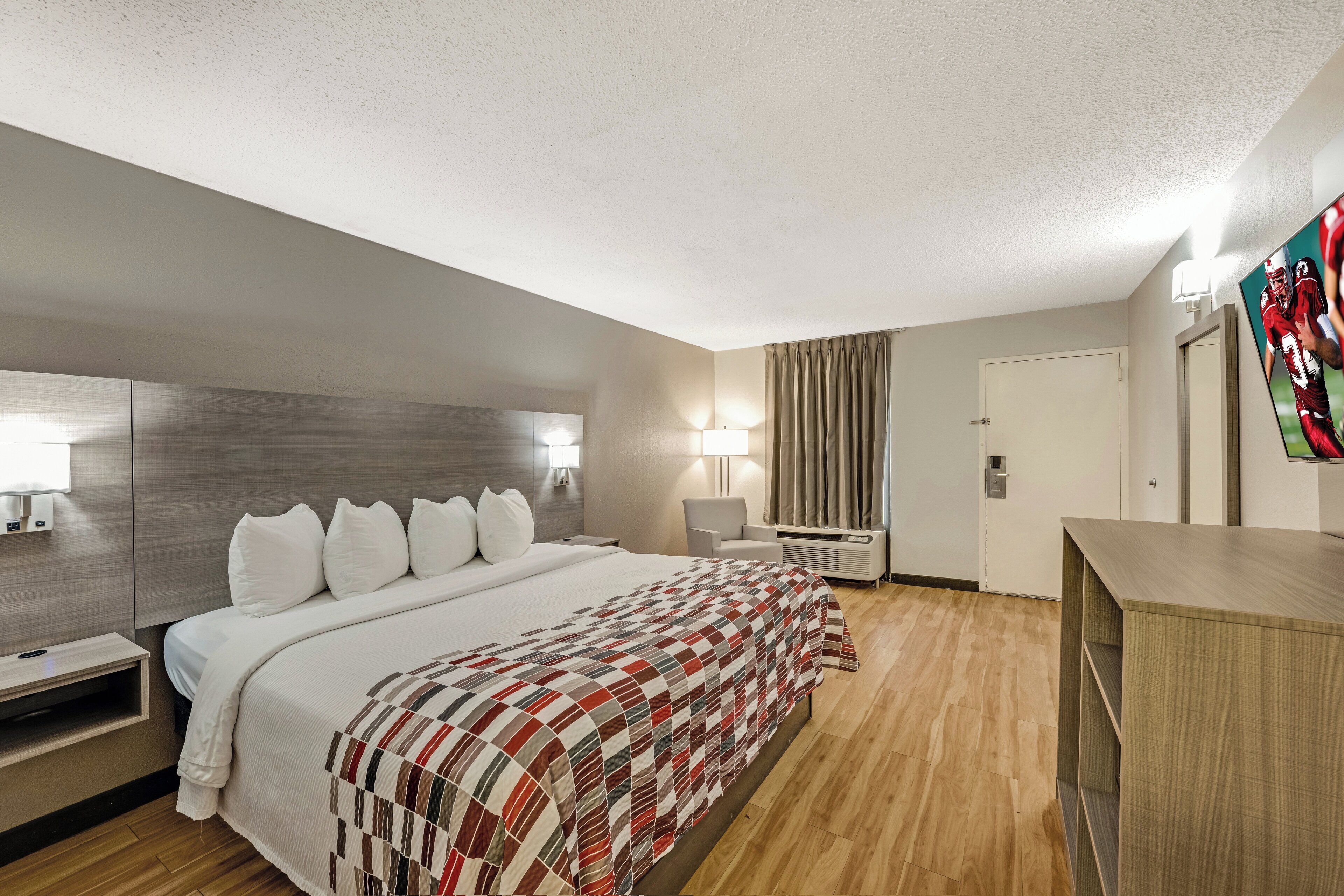 Ein Hotelzimmer mit einem großen Bett, einem Schreibtisch, einem Stuhl, einem Fernseher und einem Kleiderschrank.