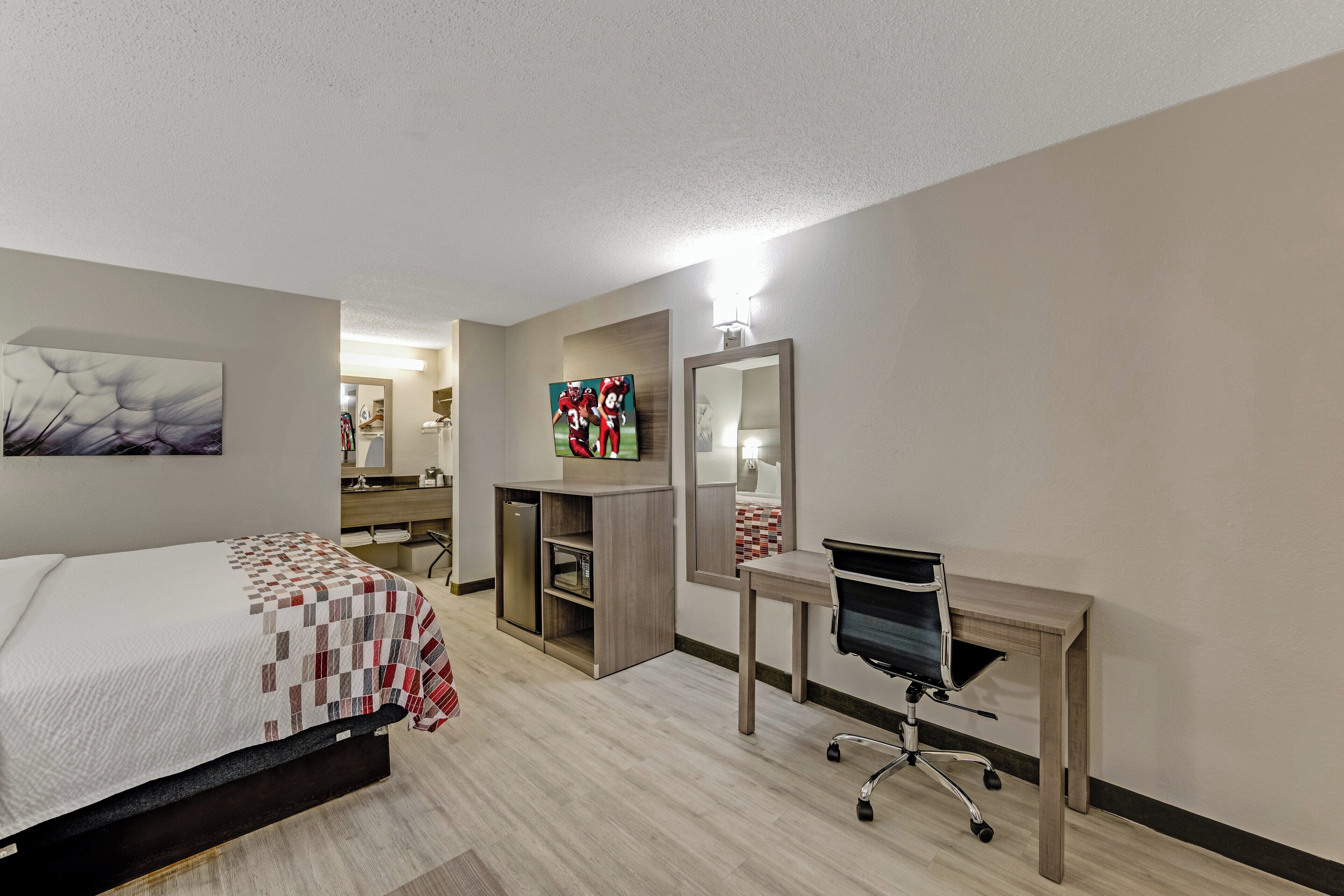 A hotel room with a bed, a desk, a chair, a mirror, and artwork on the walls.