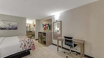 Una habitación de hotel con cama, escritorio, silla, espejo y obras de arte en las paredes.