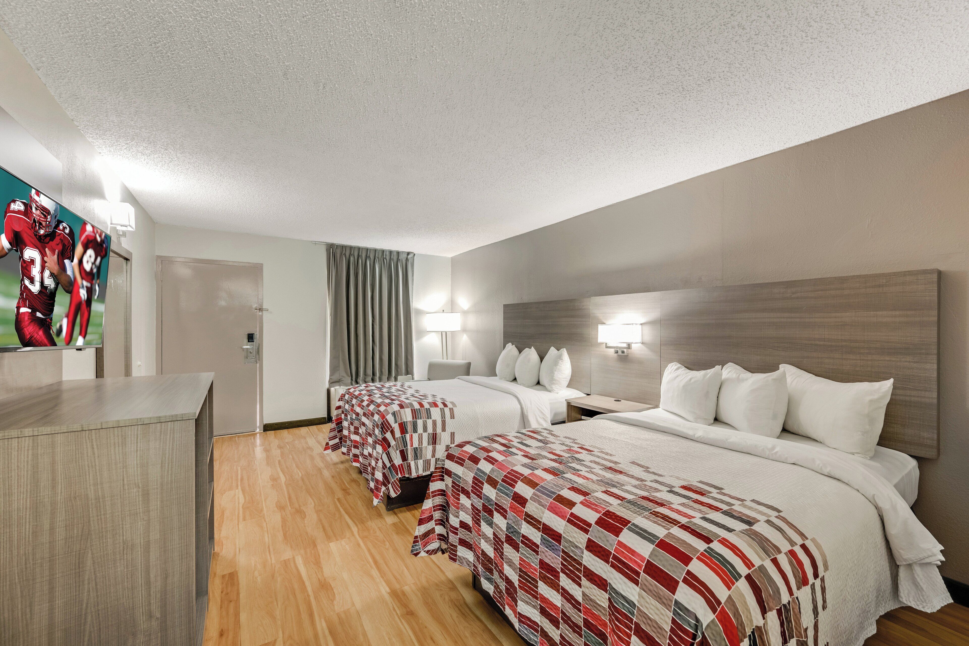 A hotel room with two beds, a desk, and a mirror.