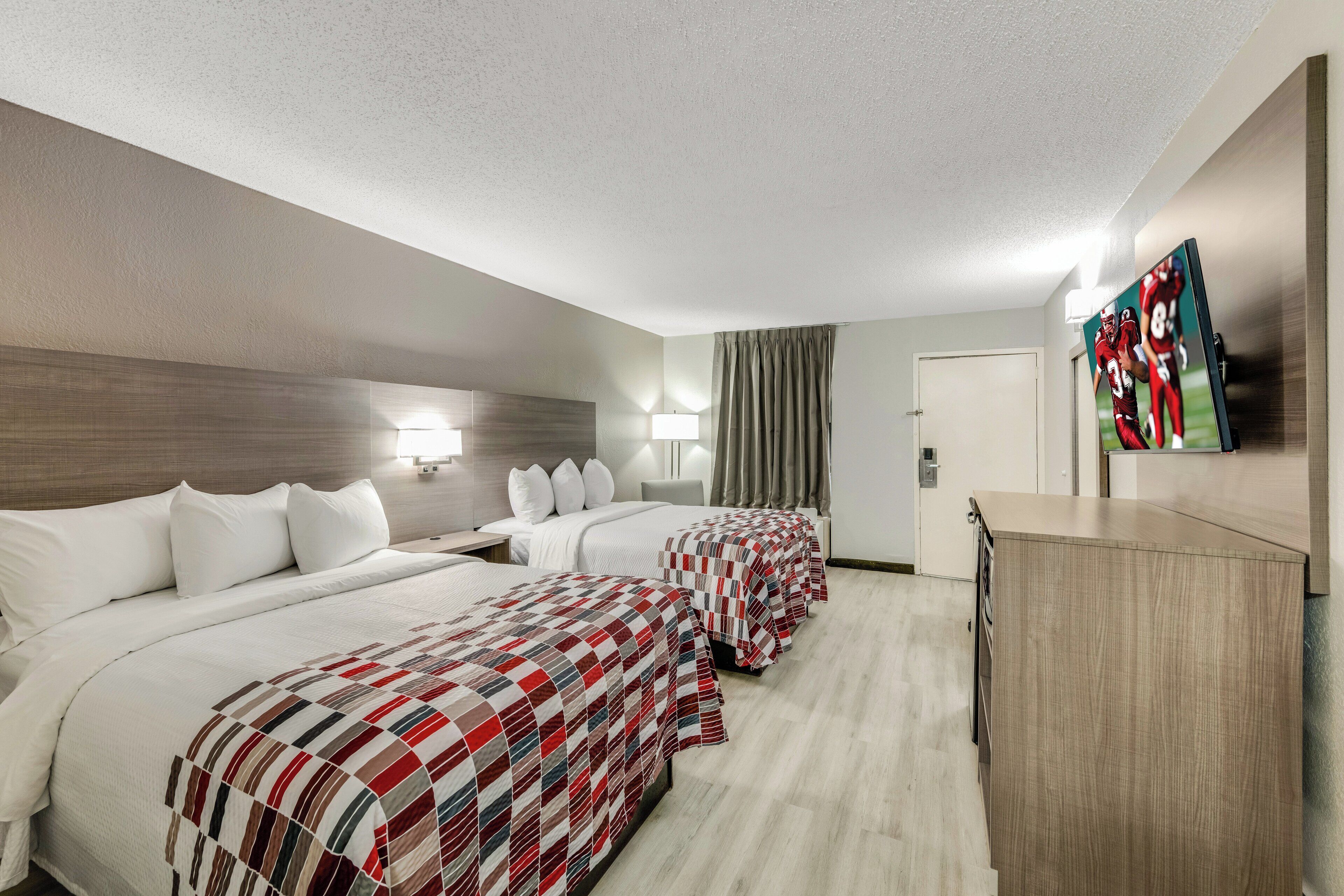 A hotel room with two beds, a desk, and a TV.