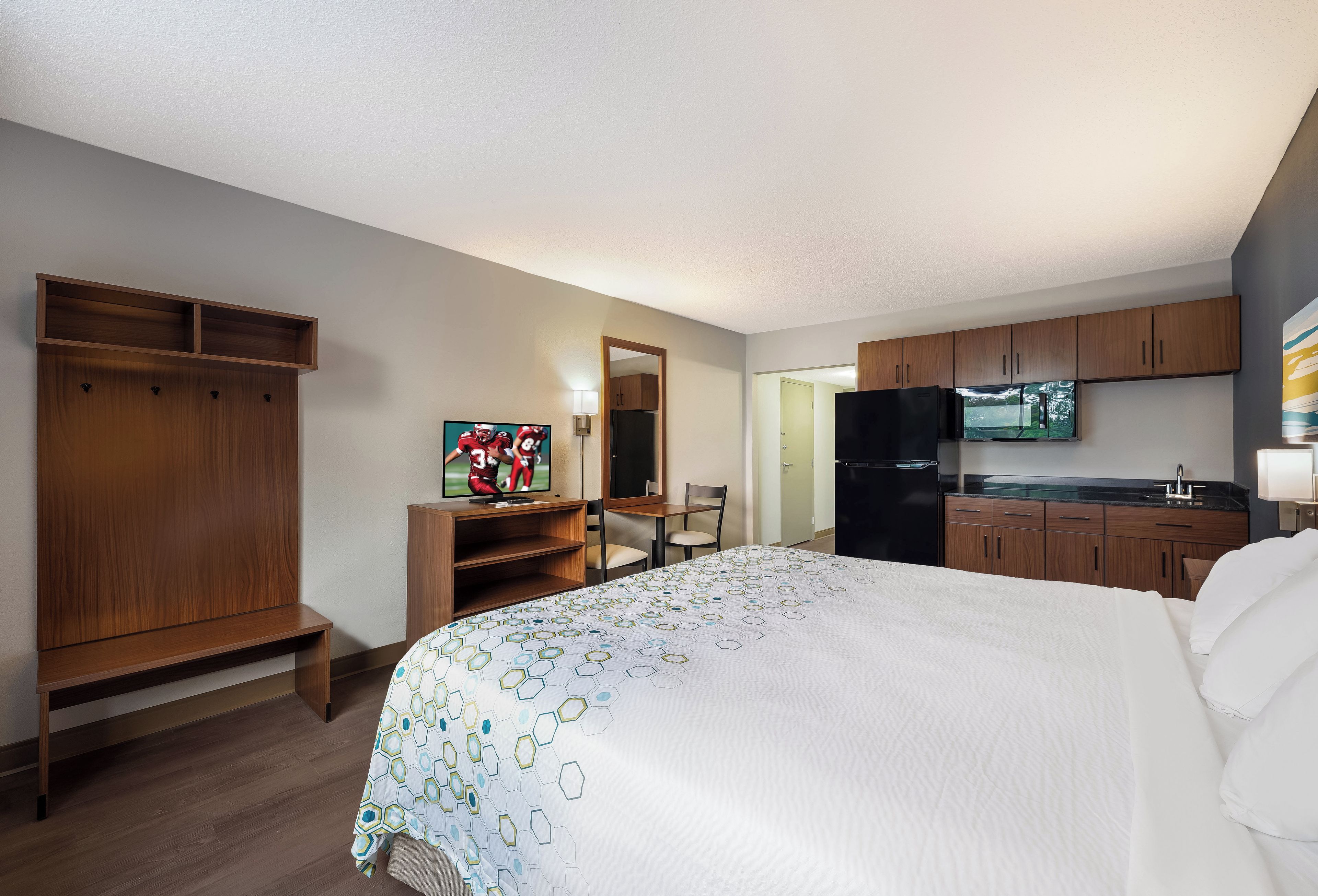 A hotel room with a bed, a TV, a desk, a chair, a wardrobe, and a kitchenette.