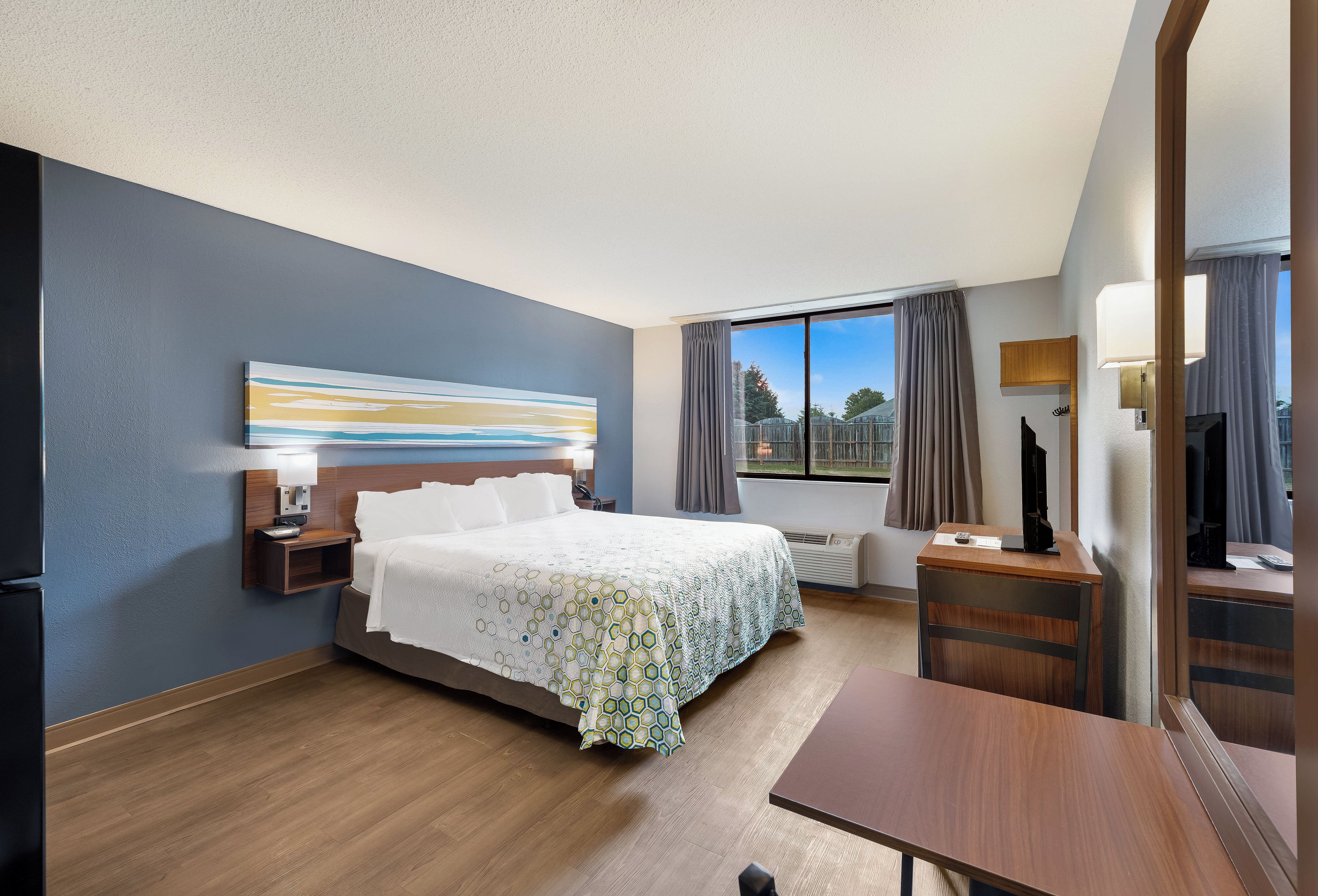 A hotel room with a bed, bedside table, lamp, and a large window with curtains.